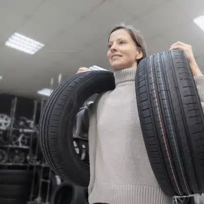 Customer lifts two car tires in showroom, comparing sizes and used tires in Waco deals