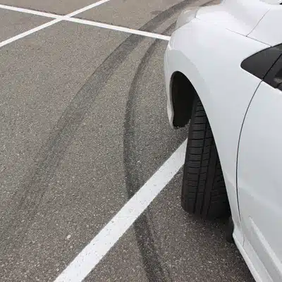 Car wheel beside parking lines with skid marks, showing tire alignment near me issue symptoms