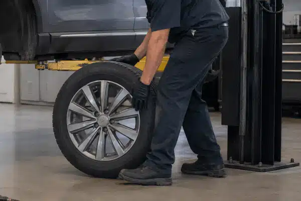 A technician removes a wheel from a lifted vehicle during routine maintenance, illustrating the labor involved in tire rotation cost